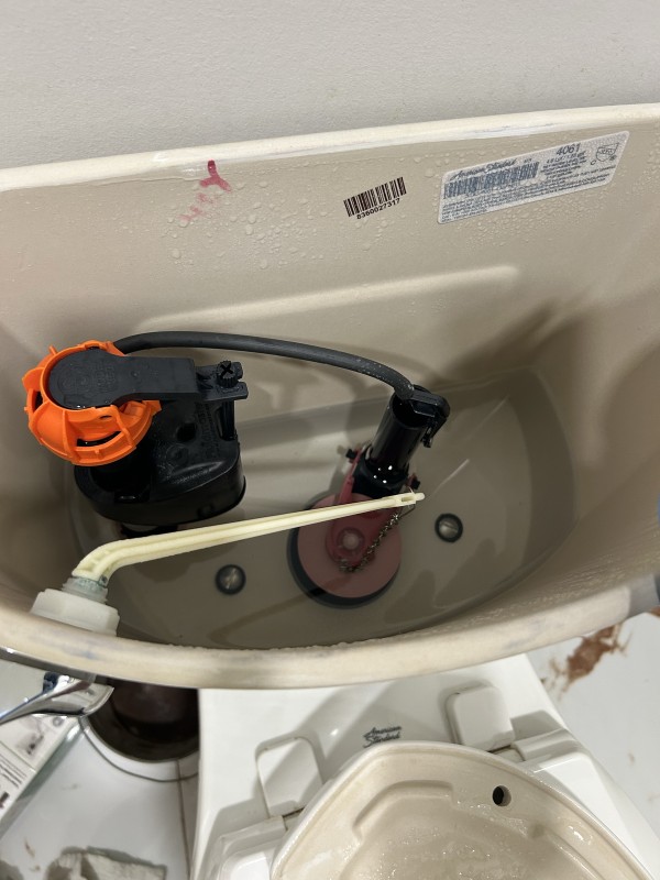 Toilet tank before repair showing old fill valve and flapper