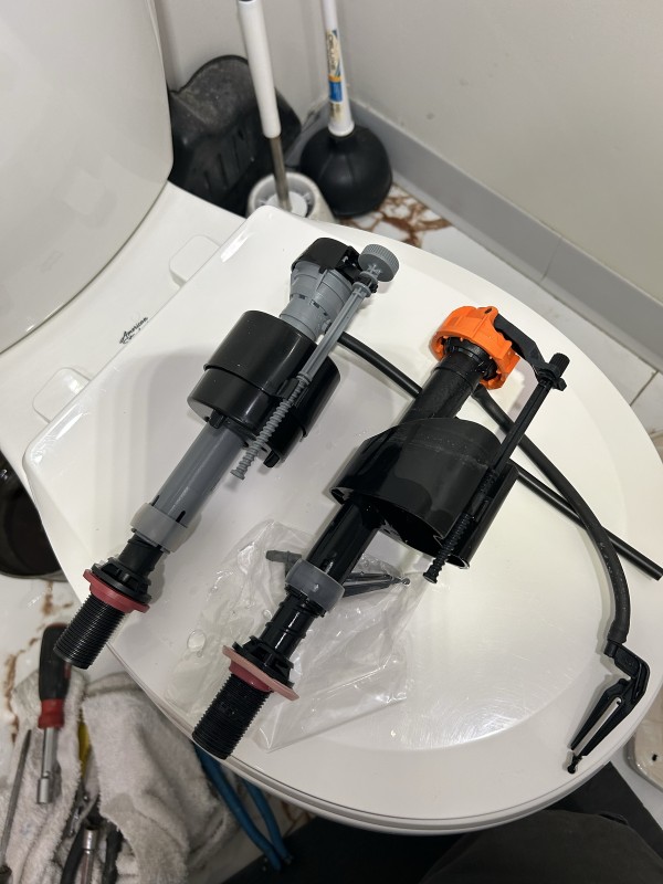 Old and new toilet fill valves side by side during plumbing repair