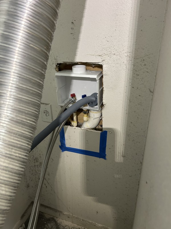 New washer box with drain pipe and water line connections being installed