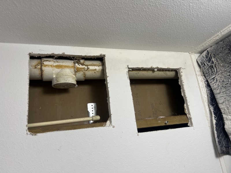 Moisture meter pressed against closet wall confirming elevated dampness