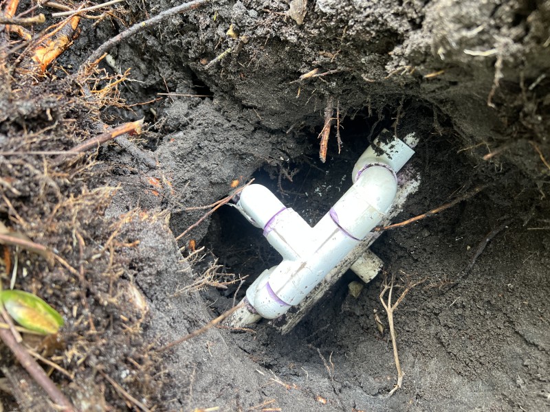 New white PVC tee with purple primer on joints installed in a small excavation