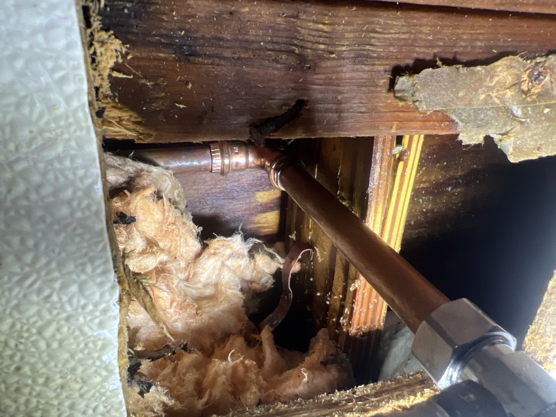 Leaking 1/2 inch copper pipe exposed behind wall before replacement