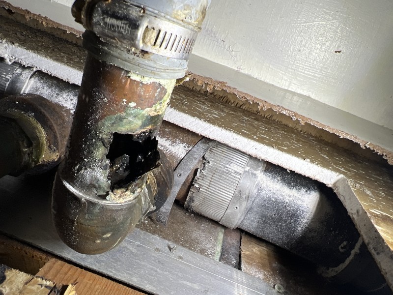 Cabinet back and drywall safely cut to expose leaking drain connection