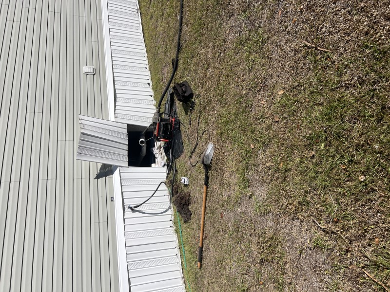 Exterior work area beside the home with plumbing tools and drain equipment staged near the skirting to create a cleanout access point, Tampa, FL, February 4, 2026