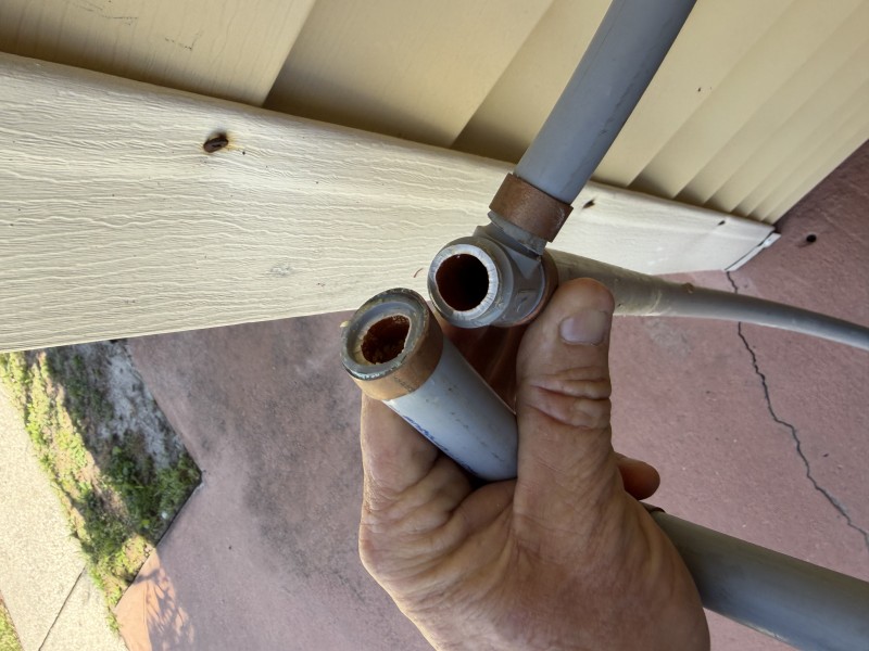 Hand holding removed section of old gray polybutylene pipe and fittings, Land O' Lakes, Florida, March 2026