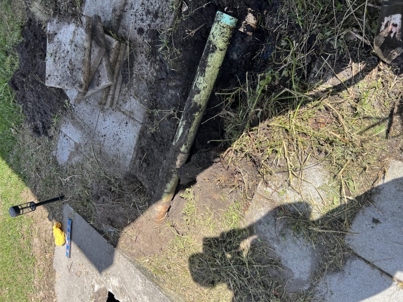 Open trench revealing the existing sagging main drain pipe buried beneath the yard surface — Polk City, FL, April 2026