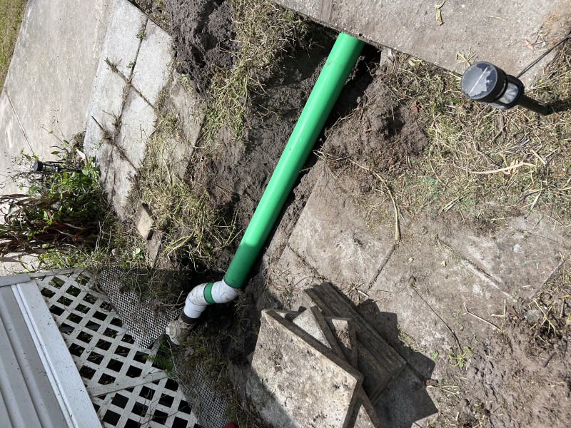 Full run of new green PVC main drain pipe showing re-piped section with correct slope and coupling connections — Polk City, FL, April 2026