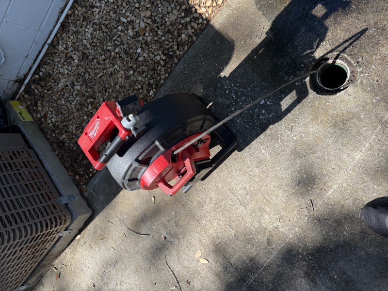 Red sewer camera inspection unit positioned on the ground next to the open exterior cleanout during post-jetting pipe inspection, South Tampa FL, April 2026