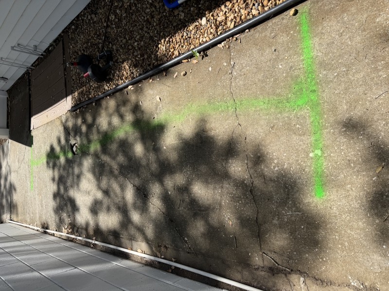 Exterior ground surface with green spray-painted utility line markings indicating the path of the main sewer line flagged for structural repair, South Tampa FL, April 2026