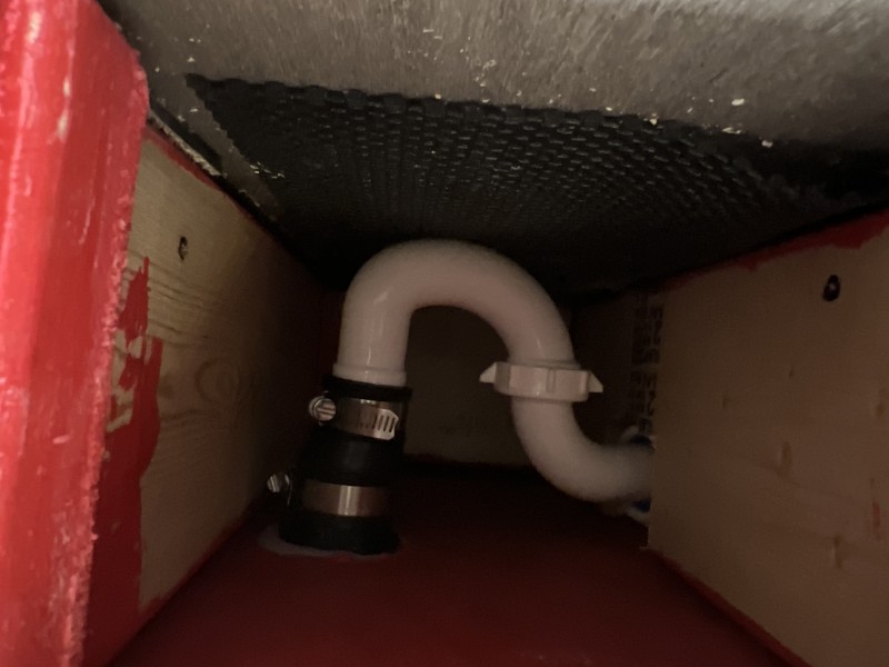 Interior view of pedicure platform cavity showing completed white PVC P-trap with black rubber Fernco coupling and stainless steel hose clamp connecting to the main drain line, Tampa FL, May 2026